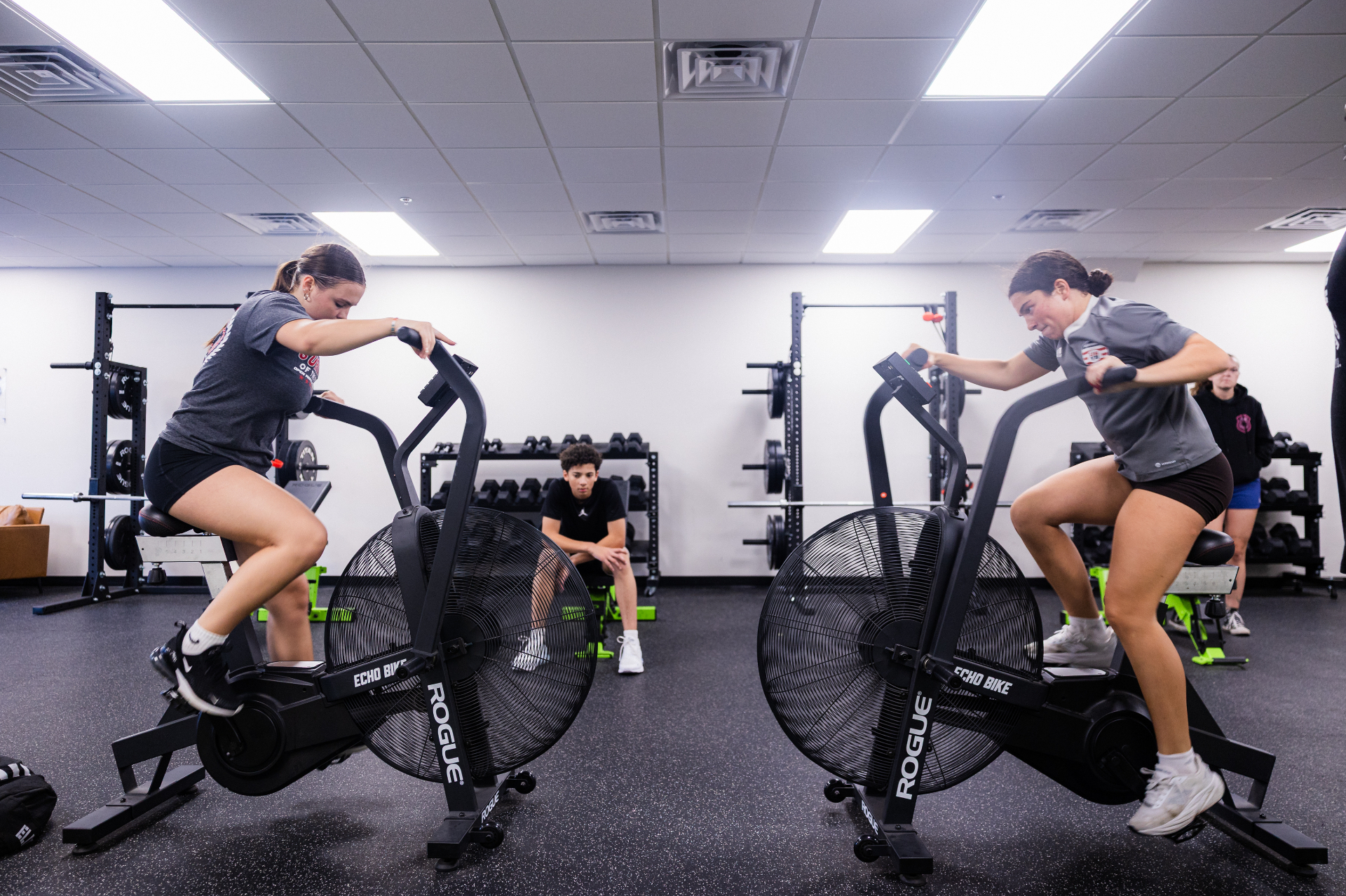 Athletes pushing through an air bike conditioning session